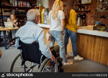 Adult disabled man in wheelchair in a queue at a cafe, disability, cafeteria interior on background. Handicapped older male person, paralyzed people in public places. Adult disabled man in wheelchair, queue at a cafe