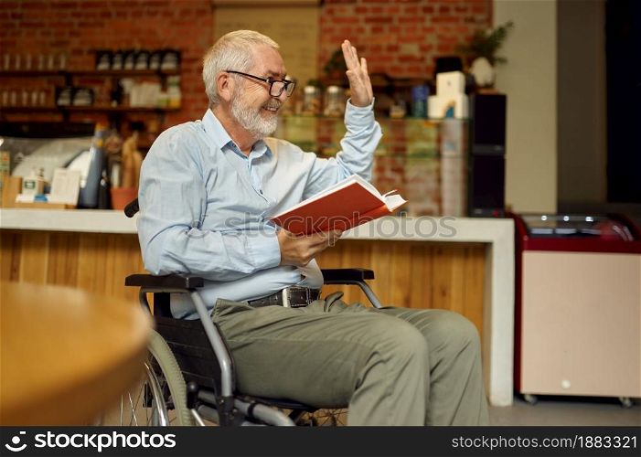 Adult disabled man in wheelchair reading a book, disability, bookshelf and university library interior on background. Handicapped older male person, paralyzed people. Adult disabled man in wheelchair reading a book