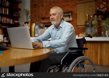 Adult disabled man in wheelchair using laptop, disability, bookshelf and university library interior on background. Handicapped older male person, paralyzed people get knowledge. Adult disabled man in wheelchair using laptop