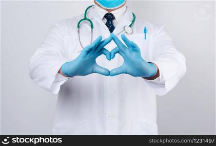 adult doctor man in a white medical coat with a stethoscope on his neck shows a heart gesture with his hands, wearing blue gloves on his hands, white background