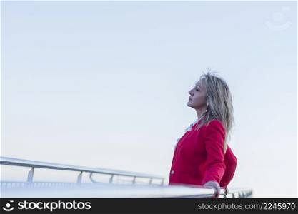 Adult female wearing red jacket relaxing while leaning on railing outdoors