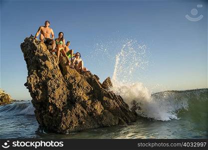Adult friends sitting on rock formation at Newport Beach, California, USA