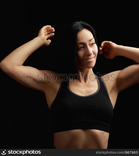 Adult girl with a sports figure in black bra standing on a dark background, muscular body, black hair