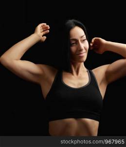 Adult girl with a sports figure in black bra standing on a dark background, muscular body, black hair