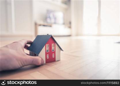 Adult hand is holding red house model, indoors. Concept for new home, property and estate