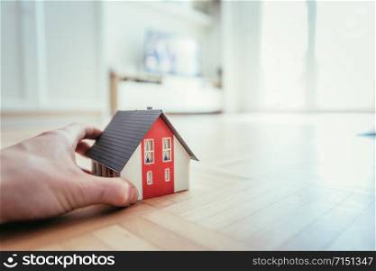 Adult hand is holding red house model, indoors. Concept for new home, property and estate