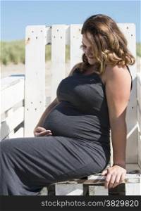 adult happy pregnant woman sitting on wooden chair on the beach