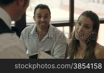 Adult hispanic couple dining out in restaurant, ordering meal and drinks and talking to bar waiter