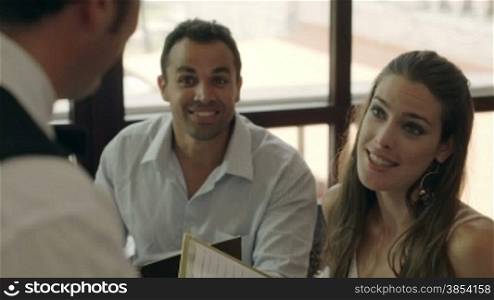Adult hispanic couple dining out in restaurant, ordering meal and drinks and talking to bar waiter