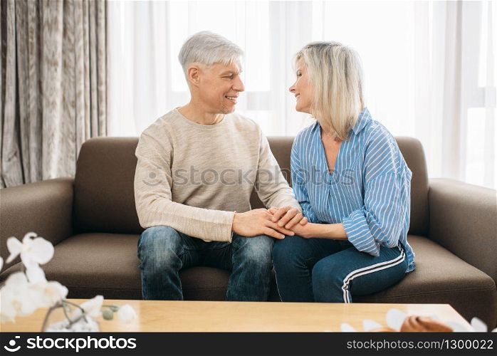 Adult love couple look each other in the eyes at home. Mature husband and wife sitting on couch and embrancing, happy family