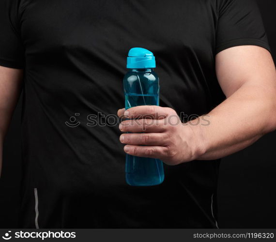 adult male athlete with muscles holds a plastic bottle of water, concept of drinking water in sports and fitness, black background. Lifestyle concept.