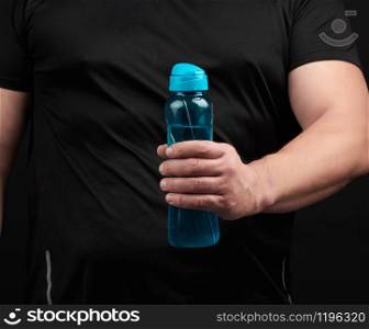 adult male athlete with muscles holds a plastic bottle of water, concept of drinking water in sports and fitness, black background. Lifestyle concept.