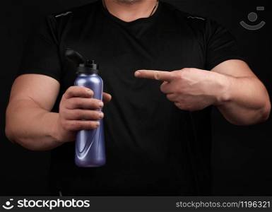 adult male athlete with muscles holds a plastic bottle of water, concept of drinking water in sports and fitness, black background