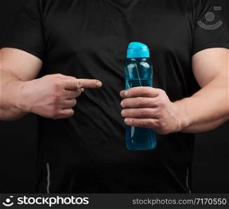 adult male athlete with muscles holds a plastic bottle of water, concept of drinking water in sports and fitness, black background