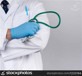 adult male doctor in a white medical coat stands and holds a green stethoscope on a white background, copy space
