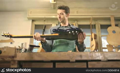 Adult man at work as artisan in workshop with bass guitar and musical instruments