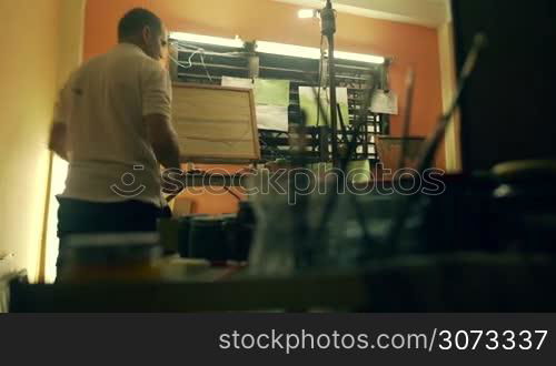 Adult man at work as sculptor chiseling a bas-relief in his atelier. He works with dentist drill on a wood painting.