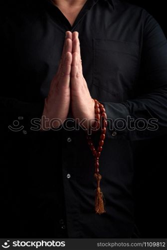 adult man in a black shirt folded his arms in front of his chest in a prayer pose, wearing brown stone rosaries on his hand, low key
