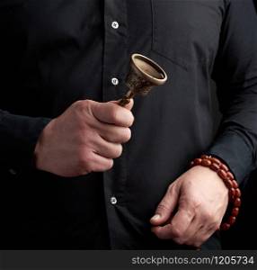 adult man in a black shirt holds a copper Tibetan ritual bell, low key. bell represents the feminine principle of excellence in wisdom.