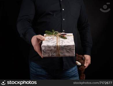 adult man in a black shirt holds a square box and brown teddy bear, concept of congratulations on Valentine&rsquo;s Day on February 14, low key