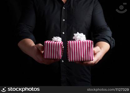 adult man in a black shirt holds in his hand a stack of paper-wrapped gifts, concept of holiday greetings, low key