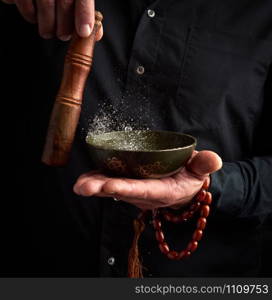 adult man in a black shirt rotates a wooden stick around a copper Tibetan bowl of water. ritual of meditation, prayers and immersion in a trance. Alternative treatment