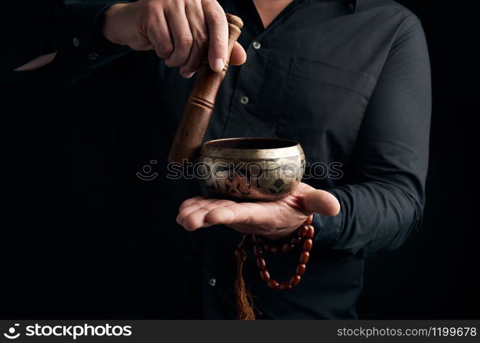 adult man in a black shirt rotates a wooden stick around a copper Tibetan bowl of water. ritual of meditation, prayers and immersion in a trance. Alternative treatment