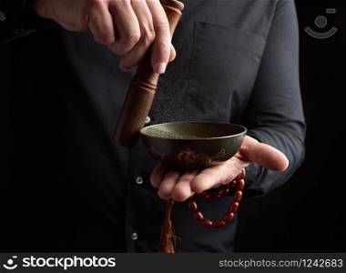 adult man in a black shirt rotates a wooden stick around a copper Tibetan bowl. ritual of meditation, prayers and immersion in a trance. Alternative treatment