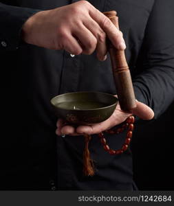 adult man in a black shirt rotates a wooden stick around a copper Tibetan bowl. ritual of meditation, prayers and immersion in a trance. Alternative treatment