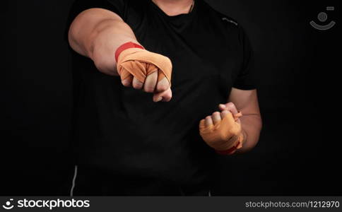 adult man in a black uniform and muscular arms stands in a sports stance, holds a sports elastic bandage on his hands, punch forward, dark background