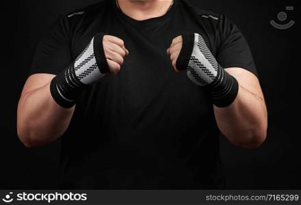 adult man in a black uniform and muscular arms stands in a sports stance, holds a sports elastic bandage on his hands, a dark background