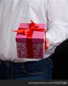 adult man in a white shirt holds a pink gift cardboard box with a bow, concept of a congratulation on the holiday, anniversary, surprise