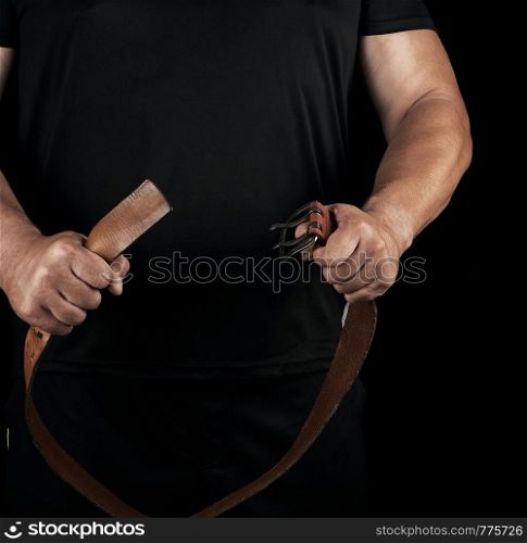 adult man in black clothes holding a brown leather belt with an iron buckle, concept of violence and aggression