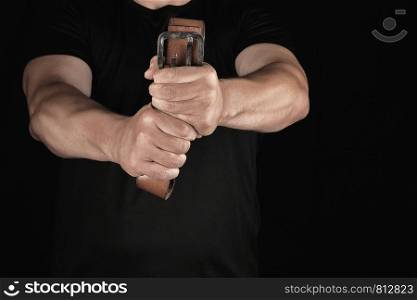 adult man in black clothes holding a brown leather belt with an iron buckle, concept of aggression