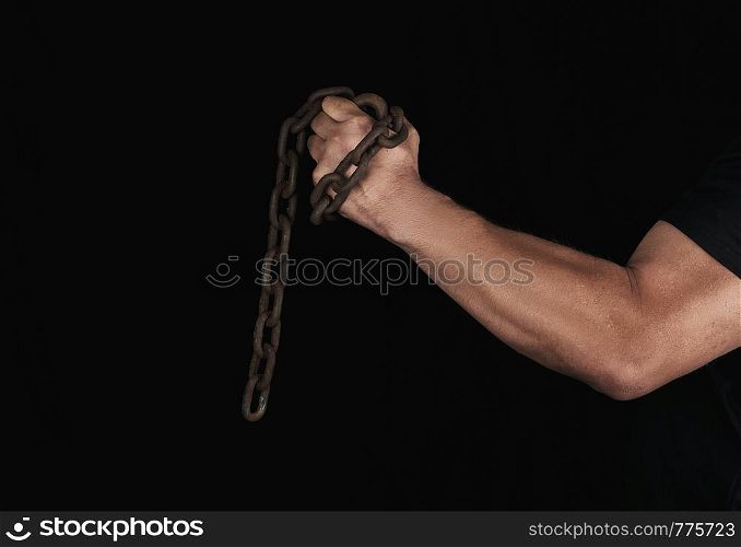 adult man in black clothes holds a brown rusty chain in his hand on a black background