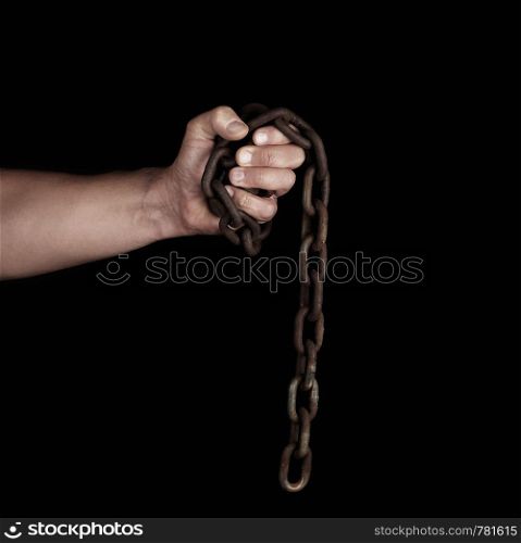 adult man in black clothes holds a brown rusty chain in his hand on a black background