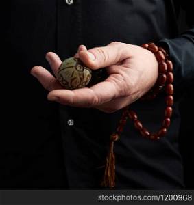 adult man in black clothes holds in his hands a stone magic ball, object for religious rituals, meditations and alternative medicine