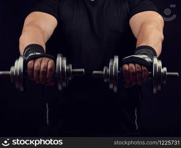adult man in black clothes holds steel dumbbells in his hands, his muscles are tense, low key, sports background