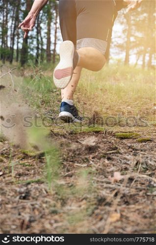 adult man in black shorts runs in the coniferous forest against the bright sun, concept of a healthy lifestyle and running in the fresh air