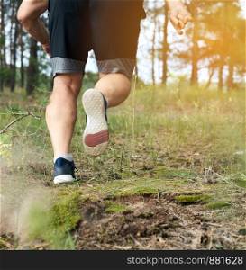 adult man in black shorts runs in the coniferous forest against the bright sun, concept of a healthy lifestyle and running in the fresh air, back view