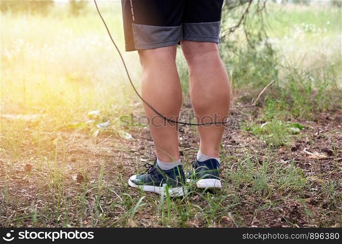 adult man in blue clothes holding a jump rope for playing sports, standing sideways against the setting sun, summer day in the middle of a coniferous forest