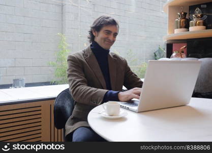 Adult man sitting in a coffee shop while drinking a cup of coffee and using a laptop