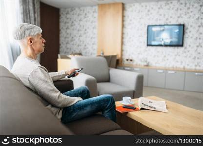 Adult man sitting on couch and watching TV at home. Mature male person in jeans relax in living room