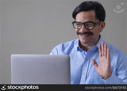 Adult man waving hand on video call through laptop