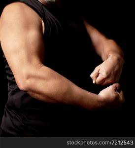 adult man with a sports figure in black clothes strained his muscles in his arms, bodybuilder shows his biceps, a low key