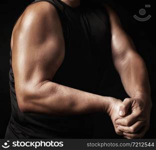 adult man with a sports figure in black clothes strained his muscles in his arms, bodybuilder shows his biceps, low key