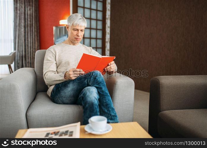 Adult man with notebook sitting on couch at home. Mature male person in jeans relax in armchair