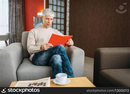 Adult man with notebook sitting on couch at home. Mature male person in jeans relax in armchair