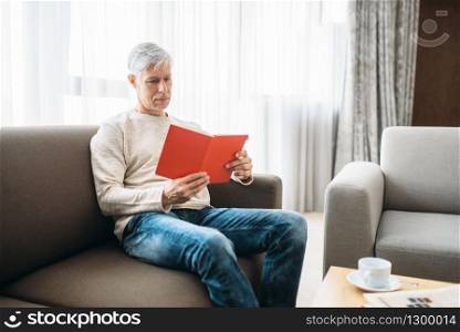 Adult man with notebook sitting on couch at home. Mature male person in jeans relax in armchair. Adult man with notebook sitting on couch at home