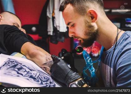 adult man working with tattoo pen arm
